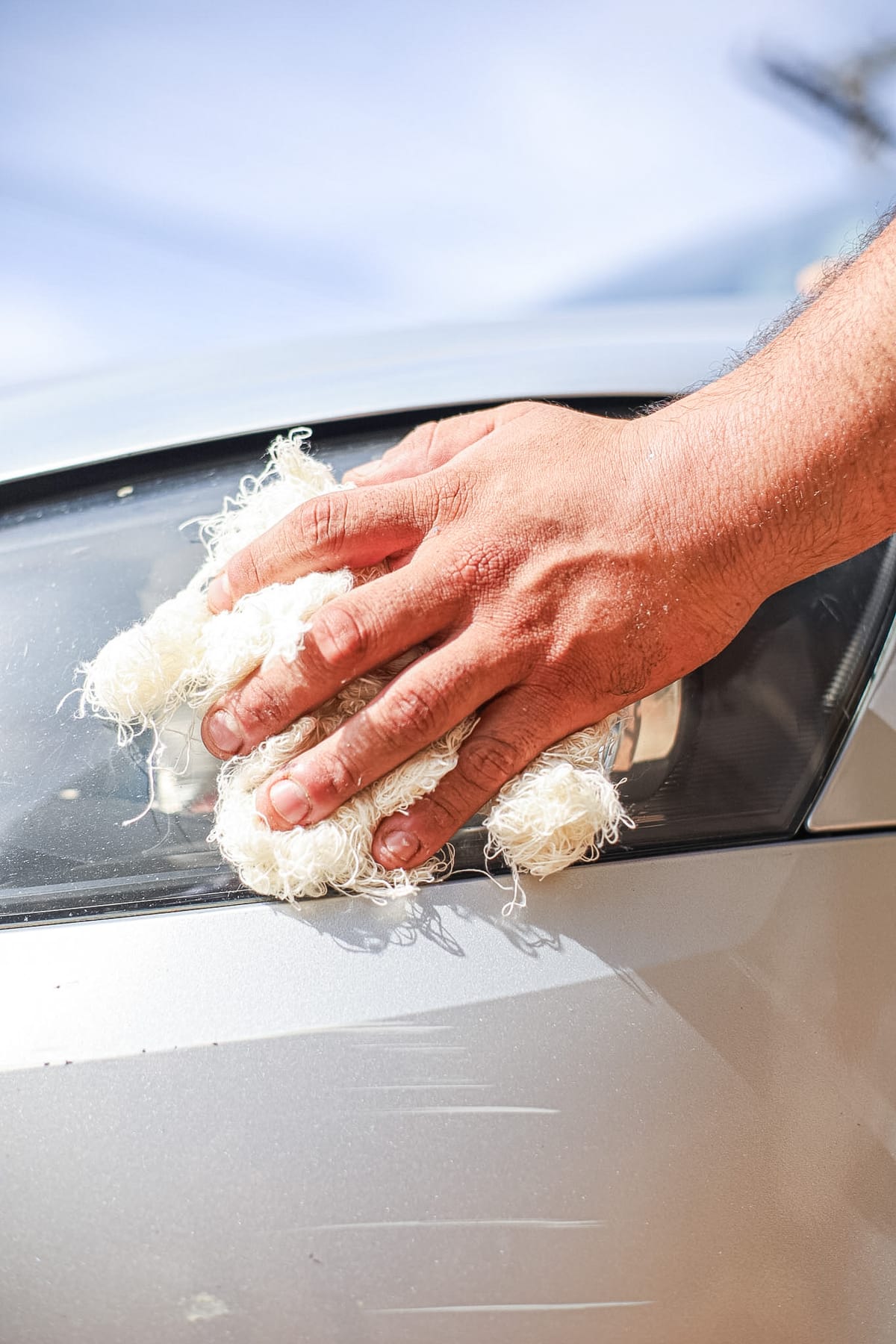 Mão usando estopa branca Bril para limpar e polir a lataria de um carro